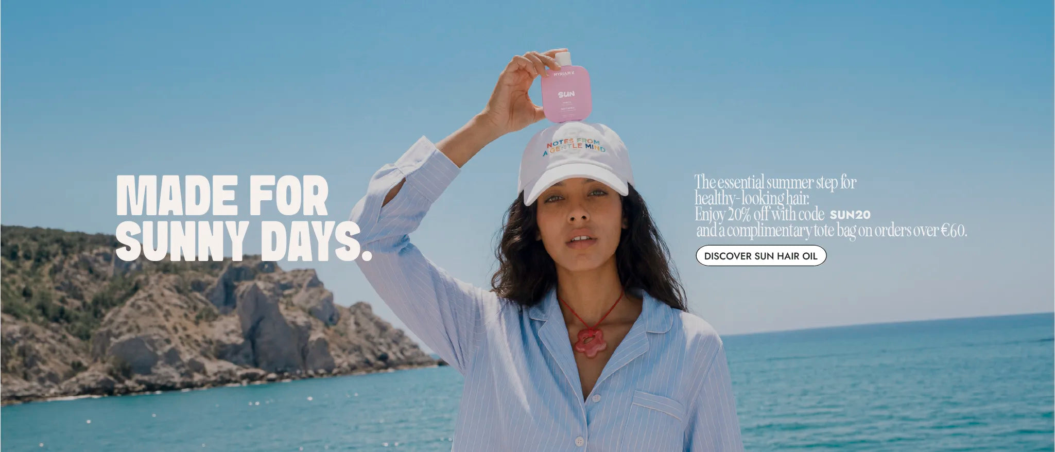 Woman holding Myriam K Paris Sun Hair Oil on a sunny beach, promoting summer hair protection with 20% off and a complimentary tote bag.